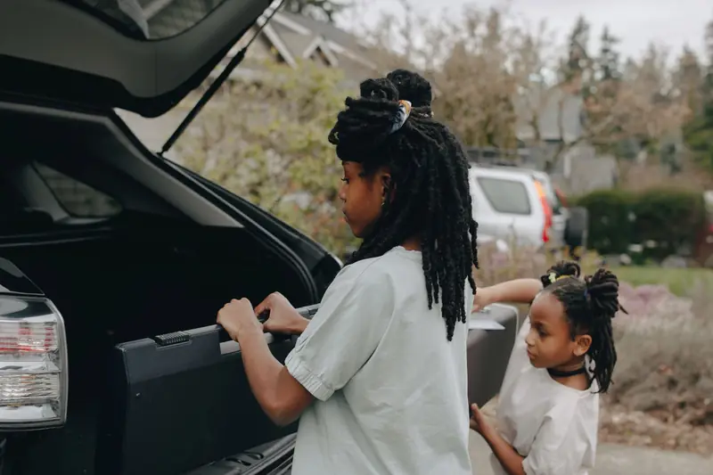 Two girls lifting luggage into the open trunk of an SUV before a family trip