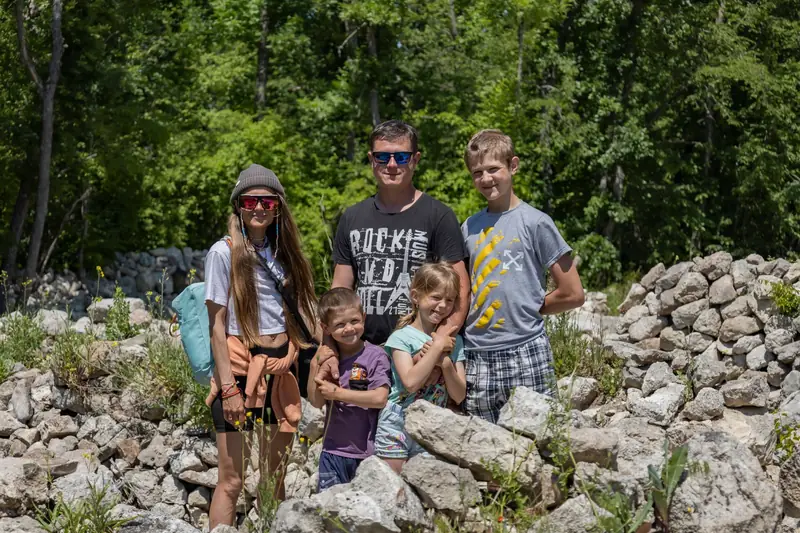 Family of five, three children and two adults, posing outdoors beside a rocky wooded hillside