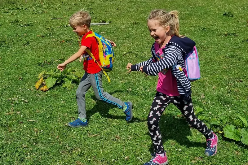 Two school-age children with backpacks running across a green meadow
